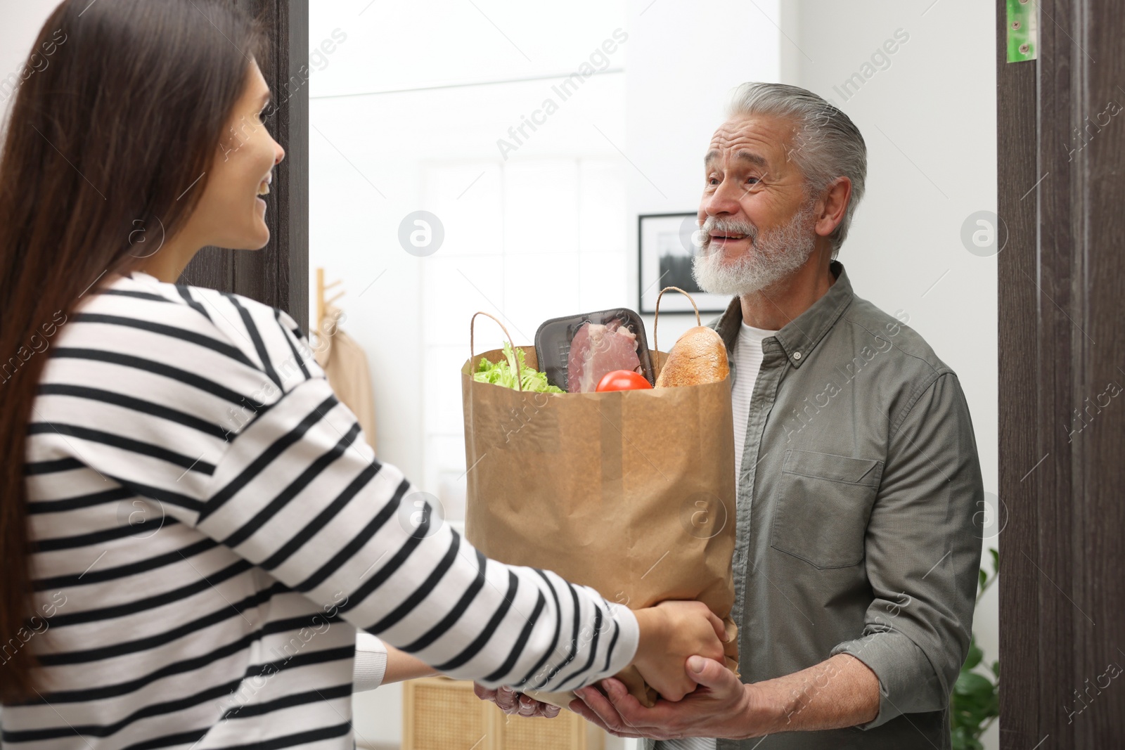 Photo of Courier giving paper bag with food products to senior man indoors