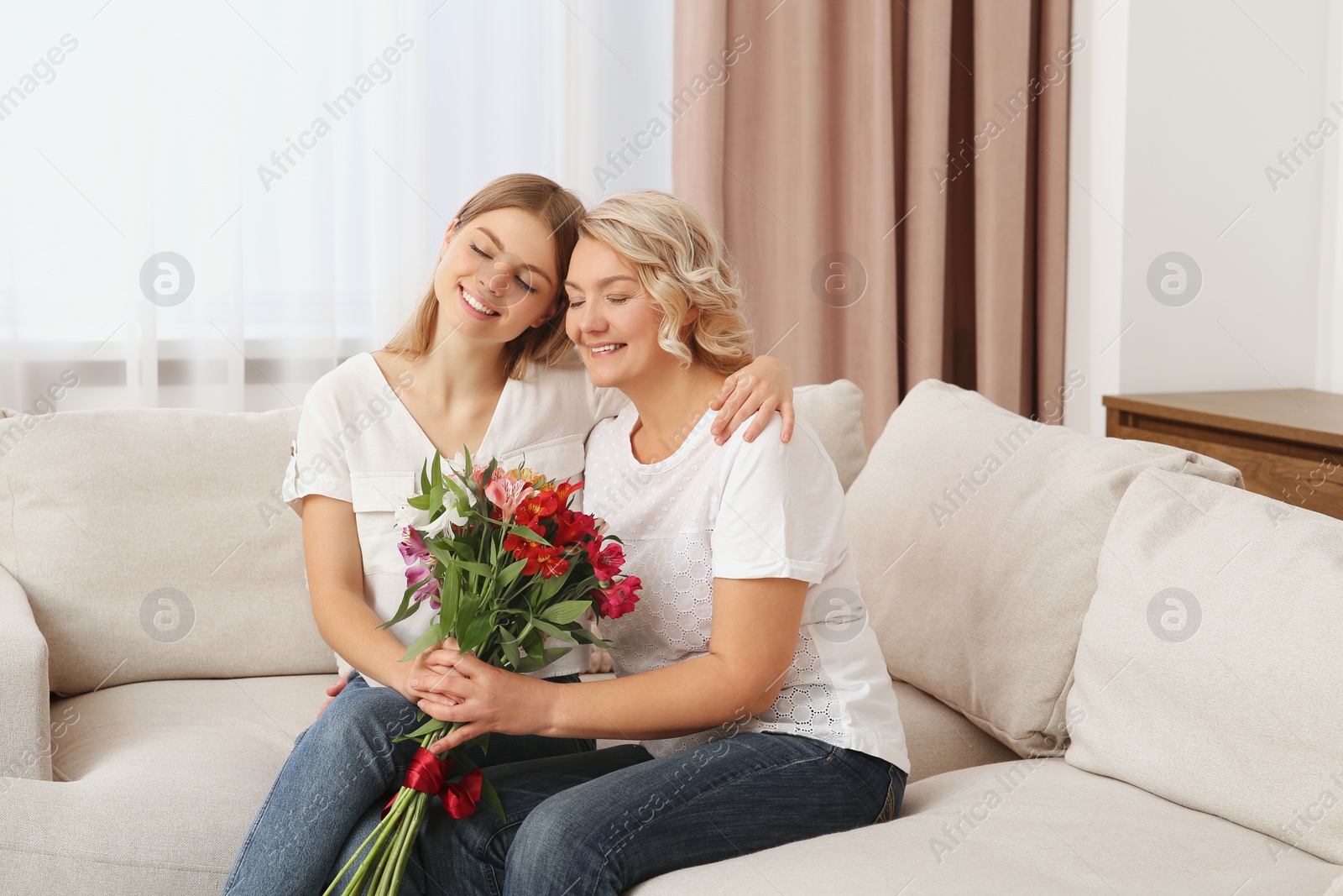 Photo of Young daughter congratulating her mom with flowers at home. Happy Mother's Day