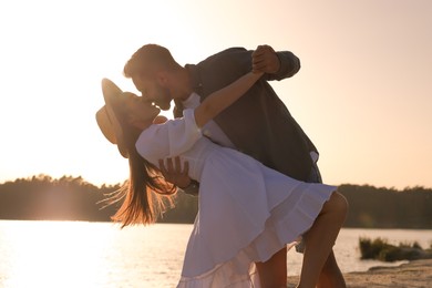 Happy couple dancing and kissing near river at sunset