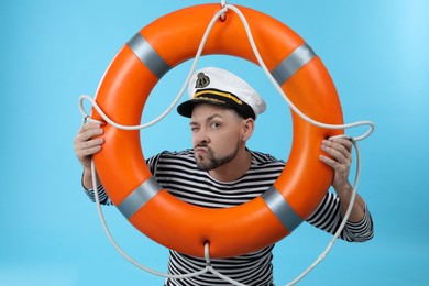 Photo of Funny sailor with orange ring buoy on light blue background