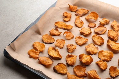 Photo of Baking sheet with sweet potato chips on grey background