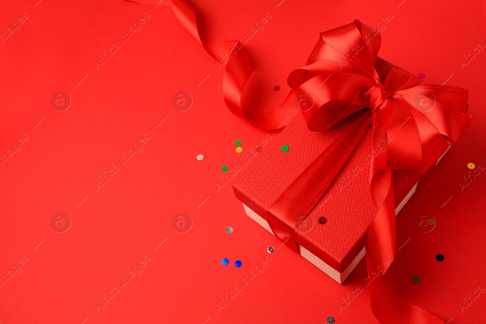 Photo of Beautiful gift box with bow and confetti on red background. Space for text