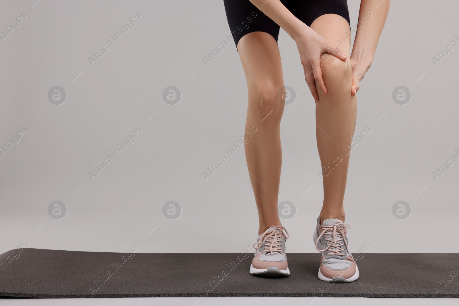 Photo of Woman suffering from leg pain on exercise mat against grey background, closeup. Space for text