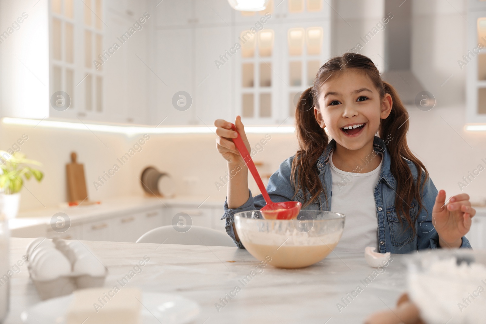 Photo of Cute little girl cooking dough at table in kitchen