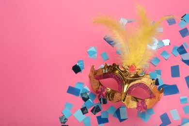 Photo of Beautiful carnival mask and shiny confetti on pink background, flat lay. Space for text