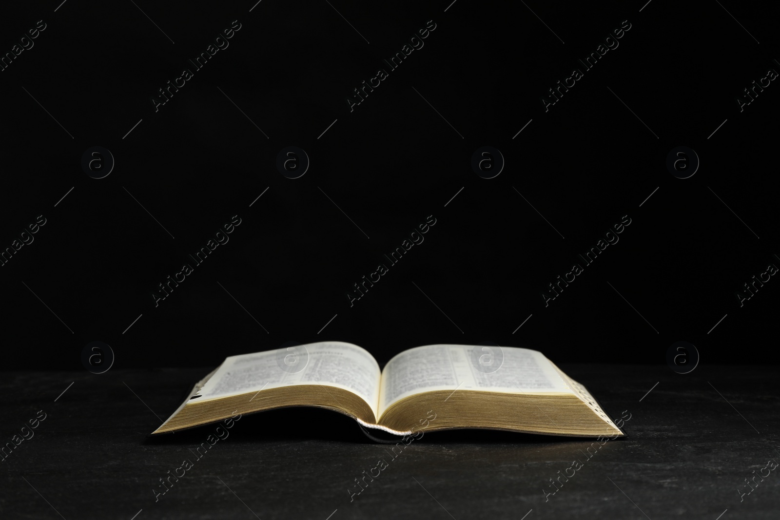 Photo of Open Bible on black table against dark background. Christian religious book