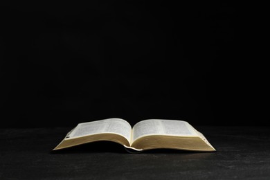 Photo of Open Bible on black table against dark background. Christian religious book