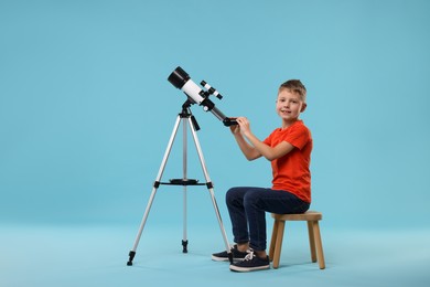 Photo of Happy little boy with telescope on light blue background