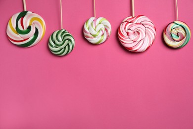 Sticks with colorful lollipops on pink background, flat lay. Space for text