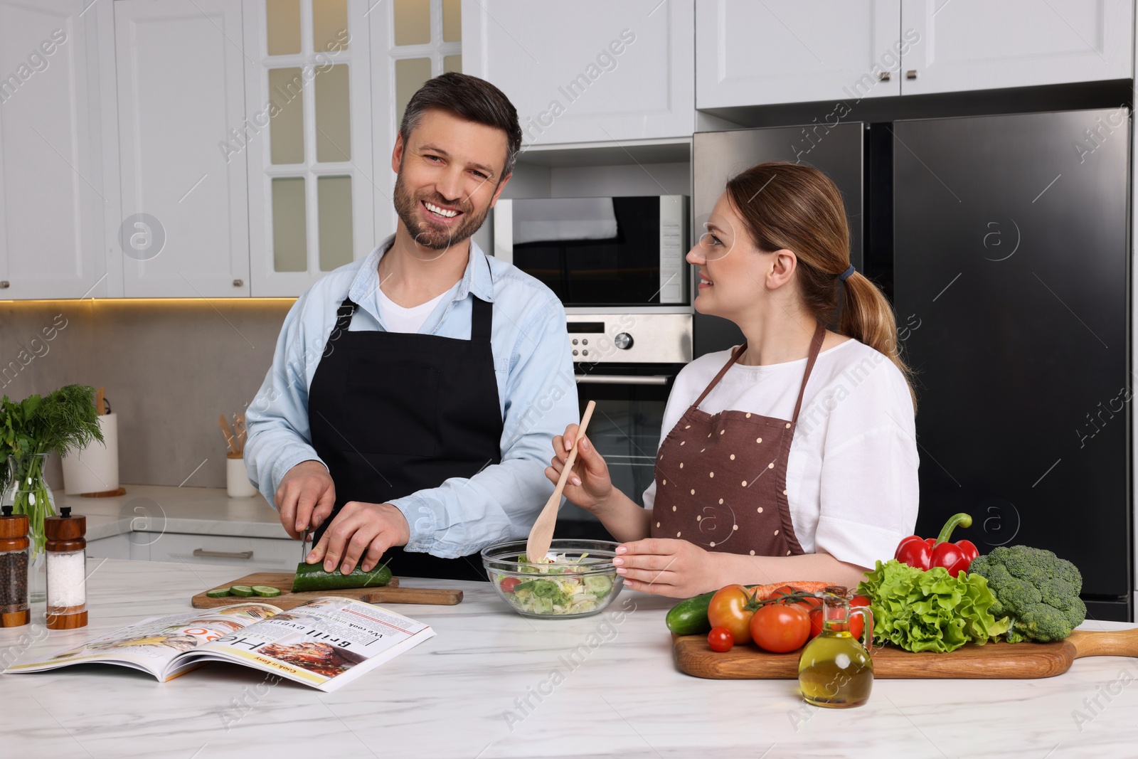 Photo of Happy couple reading recipe in culinary magazine while cooking at home