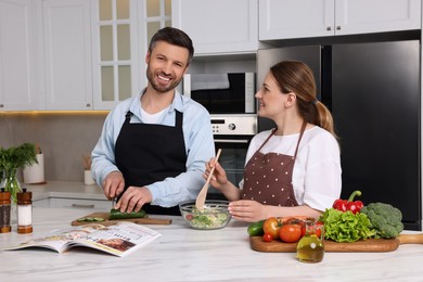 Photo of Happy couple reading recipe in culinary magazine while cooking at home