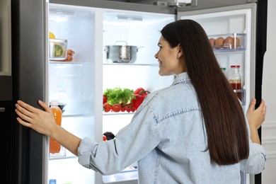 Photo of Young woman near modern refrigerator, back view