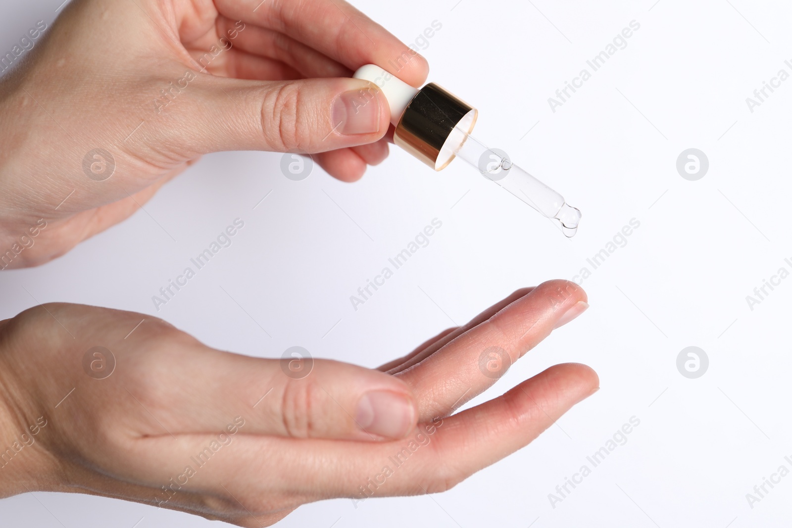 Photo of Woman applying cosmetic serum onto fingers on white background, closeup