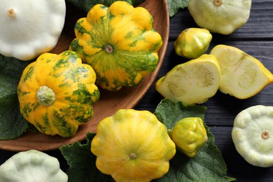 Photo of Fresh ripe pattypan squashes with leaves on black wooden table, flat lay