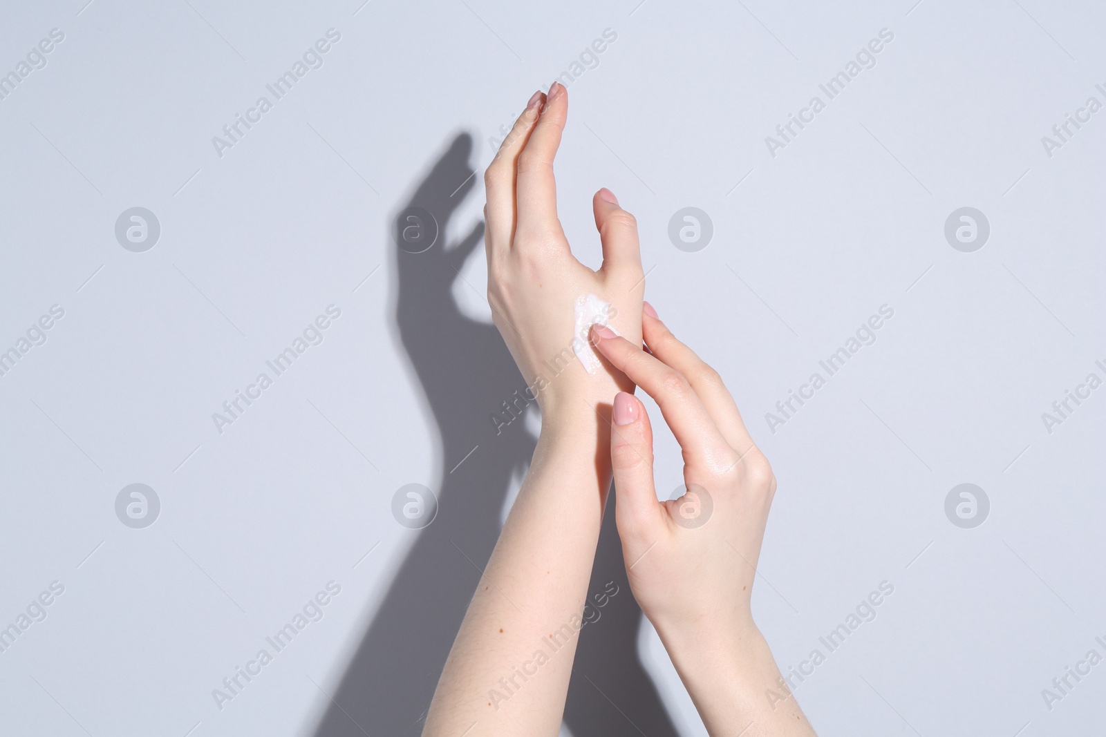 Photo of Woman applying cream on her hand against grey background, closeup