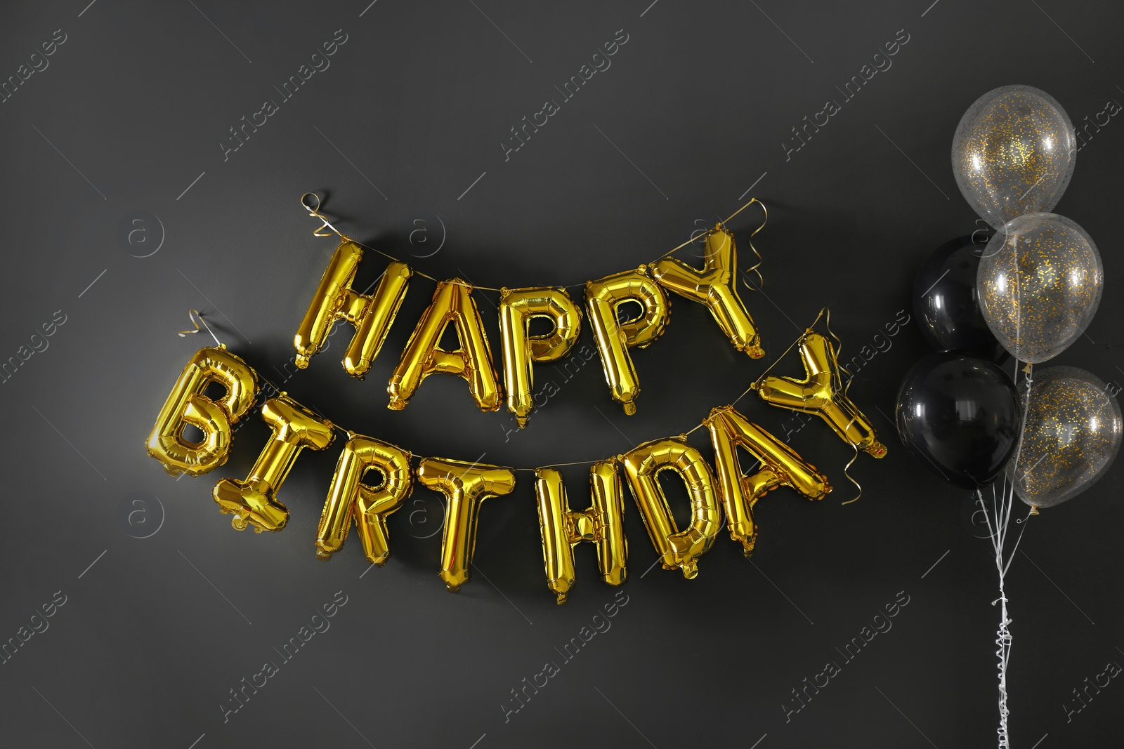 Photo of Phrase HAPPY BIRTHDAY made of golden balloon letters on black wall