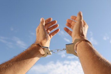 Photo of Man in handcuffs against blue sky outdoors, closeup