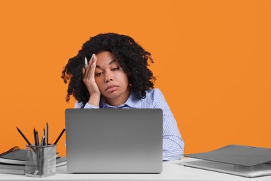 Photo of Stressful deadline. Tired woman looking at laptop at white table on orange background