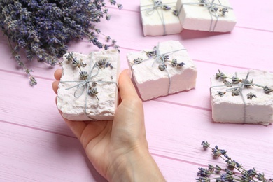 Woman holding hand made soap bar with lavender flowers on pink wooden background, closeup