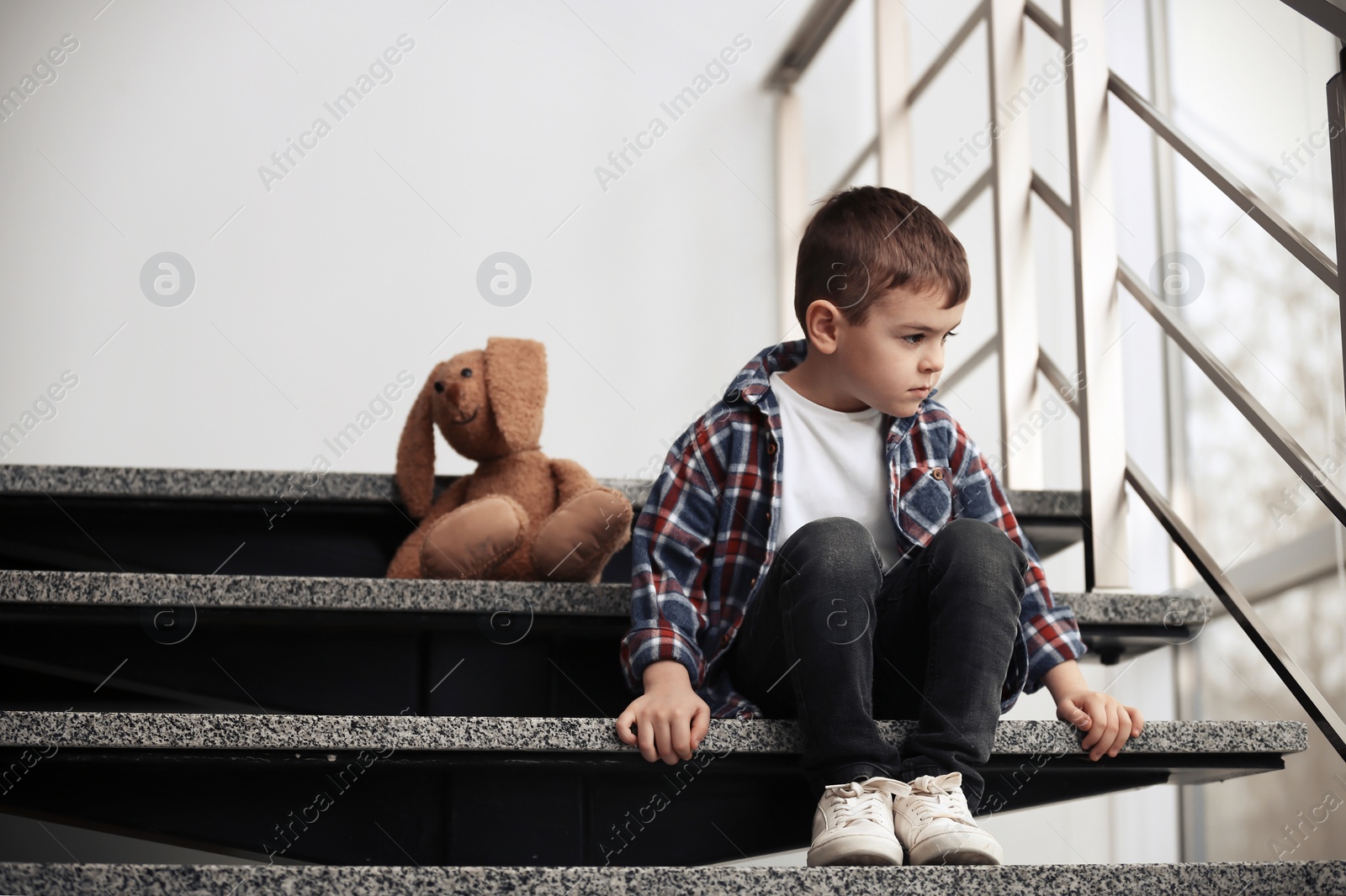 Photo of Sad little boy with toy sitting on stairs indoors