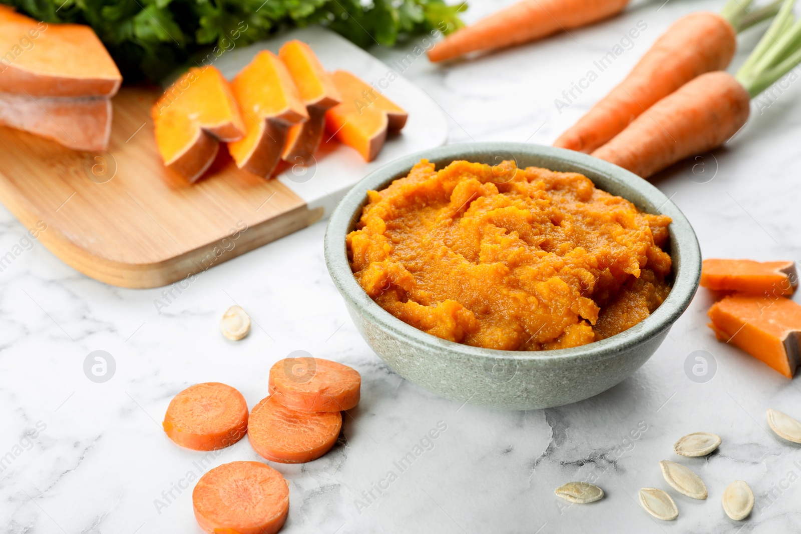 Photo of Tasty puree in bowl and ingredients on white marble table