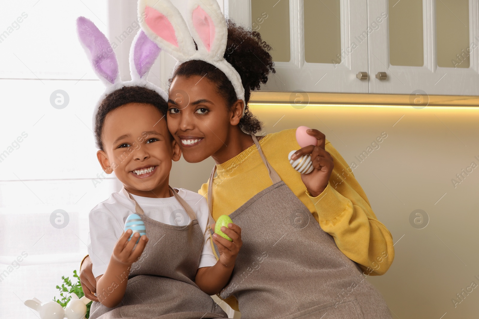 Photo of Happy African American mother and her cute son with Easter eggs in kitchen