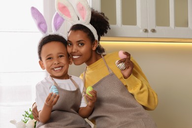 Photo of Happy African American mother and her cute son with Easter eggs in kitchen