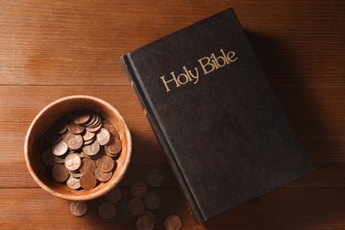Donate and give concept. Coins in bowl and Bible on wooden table, flat lay