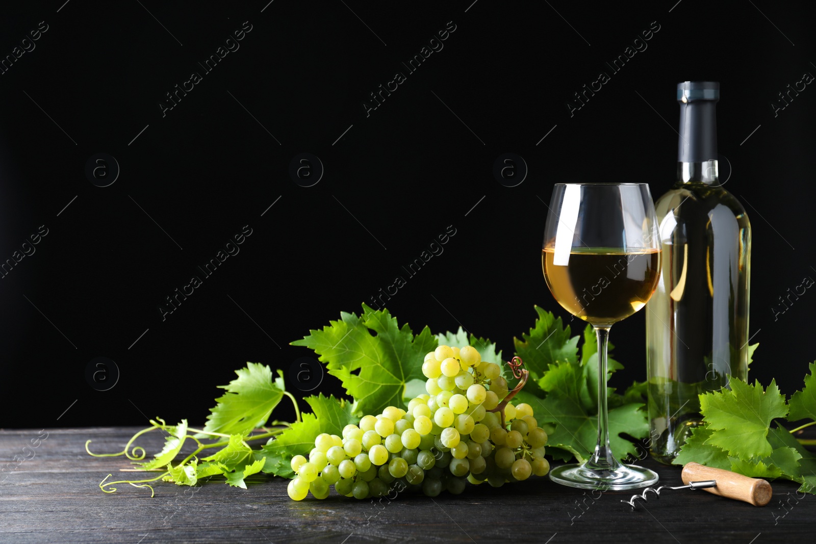 Photo of Fresh ripe juicy grapes with wineglass on grey table against black background, space for text