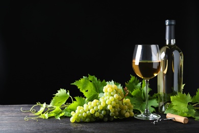 Fresh ripe juicy grapes with wineglass on grey table against black background, space for text