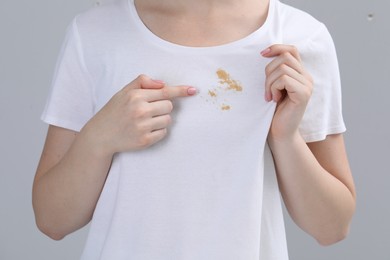 Woman showing stain on her t-shirt against light grey background, closeup