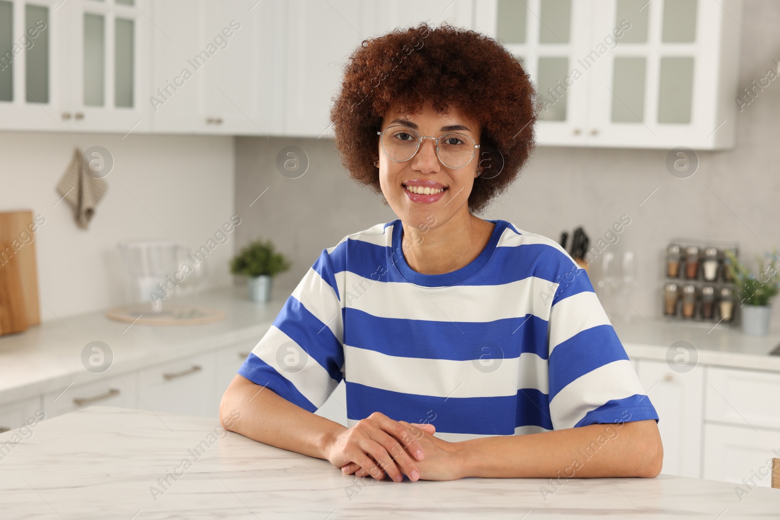 Photo of Happy young woman sitting at table in kitchen