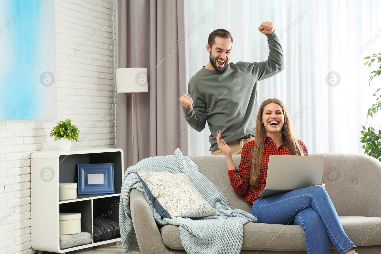 Photo of Emotional young couple with laptop celebrating victory at home