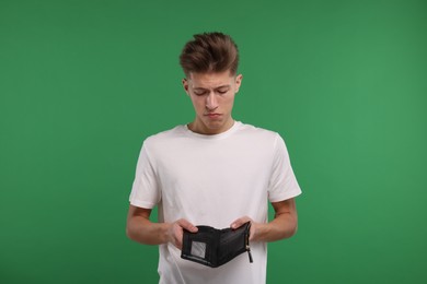 Upset man with empty wallet on green background