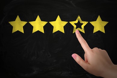 Quality evaluation. Woman touching golden star on black chalkboard, closeup