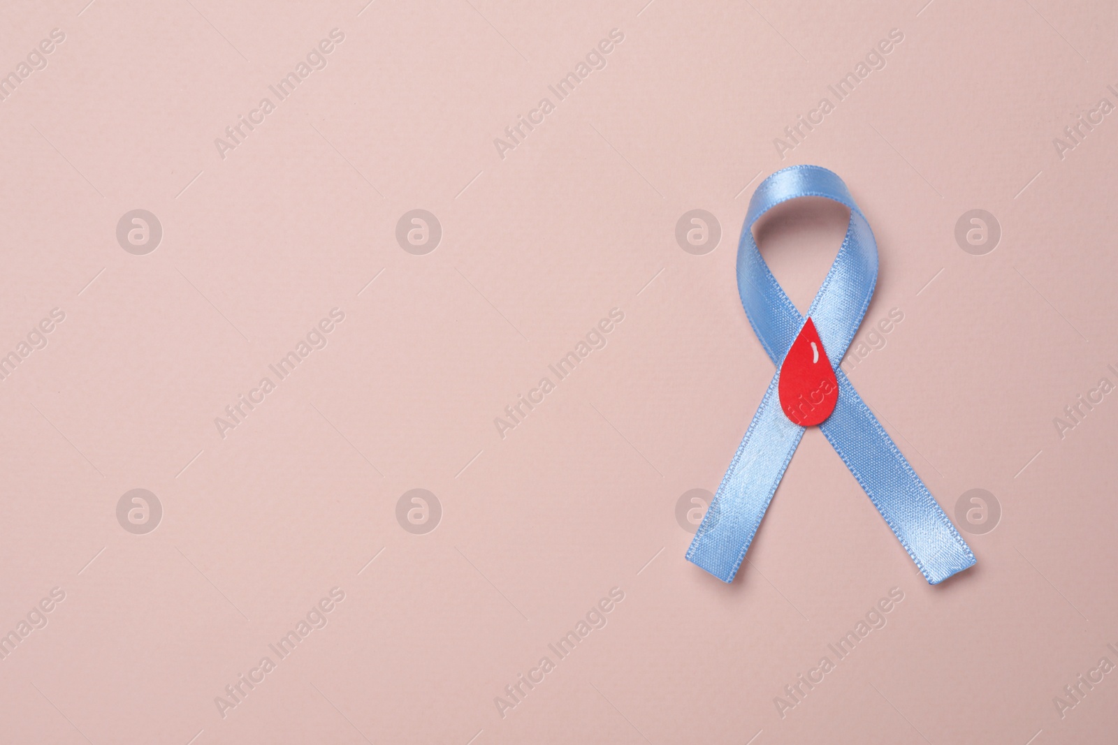 Photo of Light blue ribbon with paper blood drop on pale pink background, top view and space for text. Diabetes awareness