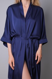 Woman in beautiful dark blue silk robe on grey background, closeup