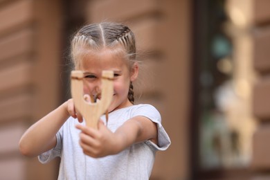 Photo of Little girl playing with slingshot outdoors. Space for text