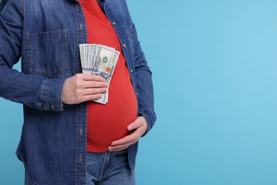 Surrogate mother. Pregnant woman with dollar banknotes on light blue background, closeup. Space for text