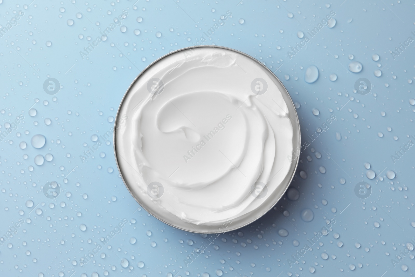 Photo of Jar of face cream on light blue surface covered with water drops, top view