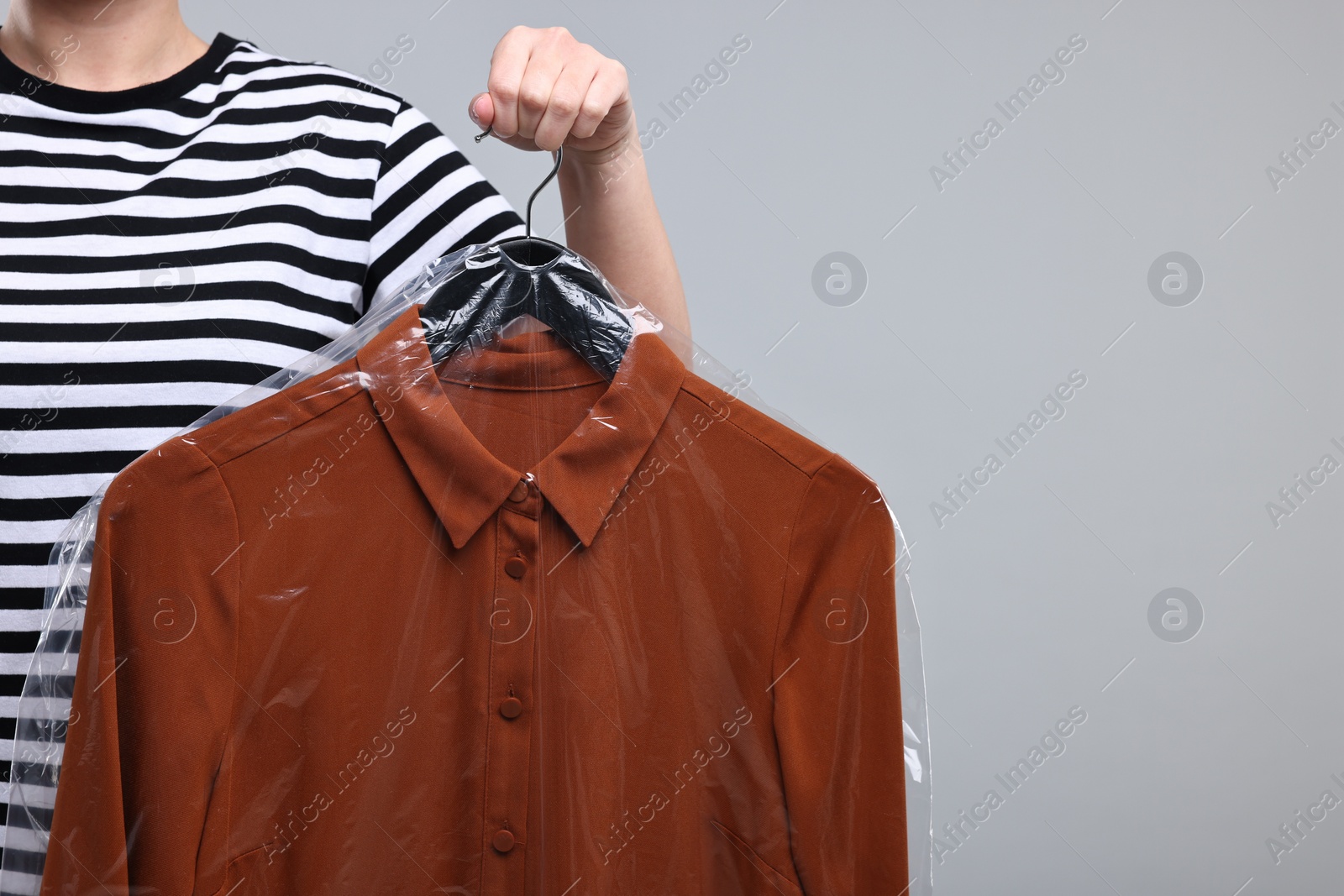 Photo of Dry-cleaning service. Woman holding shirt in plastic bag on gray background, closeup. Space for text