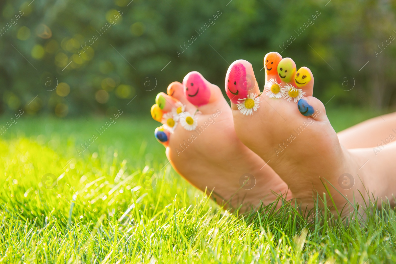 Photo of Teenage girl with drawn smiling faces and chamomiles between toes outdoors, closeup. Space for text