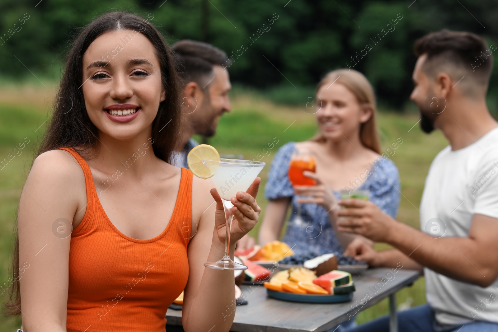 Photo of Friends having cocktail party outdoors. Happy woman with glass of drink, selective focus