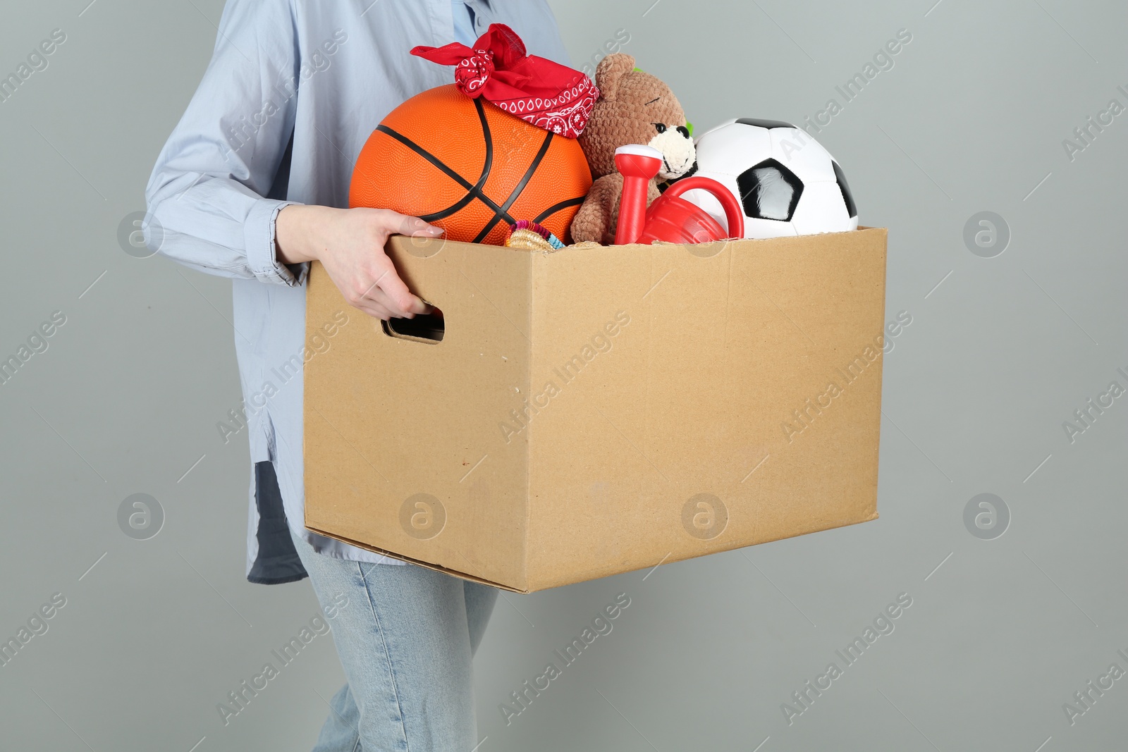 Photo of Woman holding box of unwanted stuff on grey background, closeup