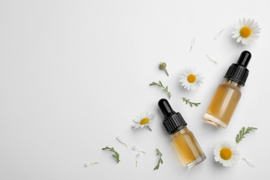 Composition with chamomile flowers and cosmetic bottles of essential oil on white background, top view