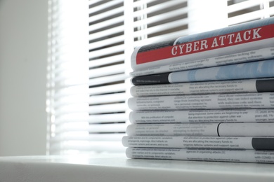 Newspapers with headline CYBER ATTACK stacked on white table indoors. Space for text