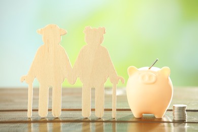 Pension savings. Figure of senior couple, piggy bank and stacked coins on wooden table against blurred background