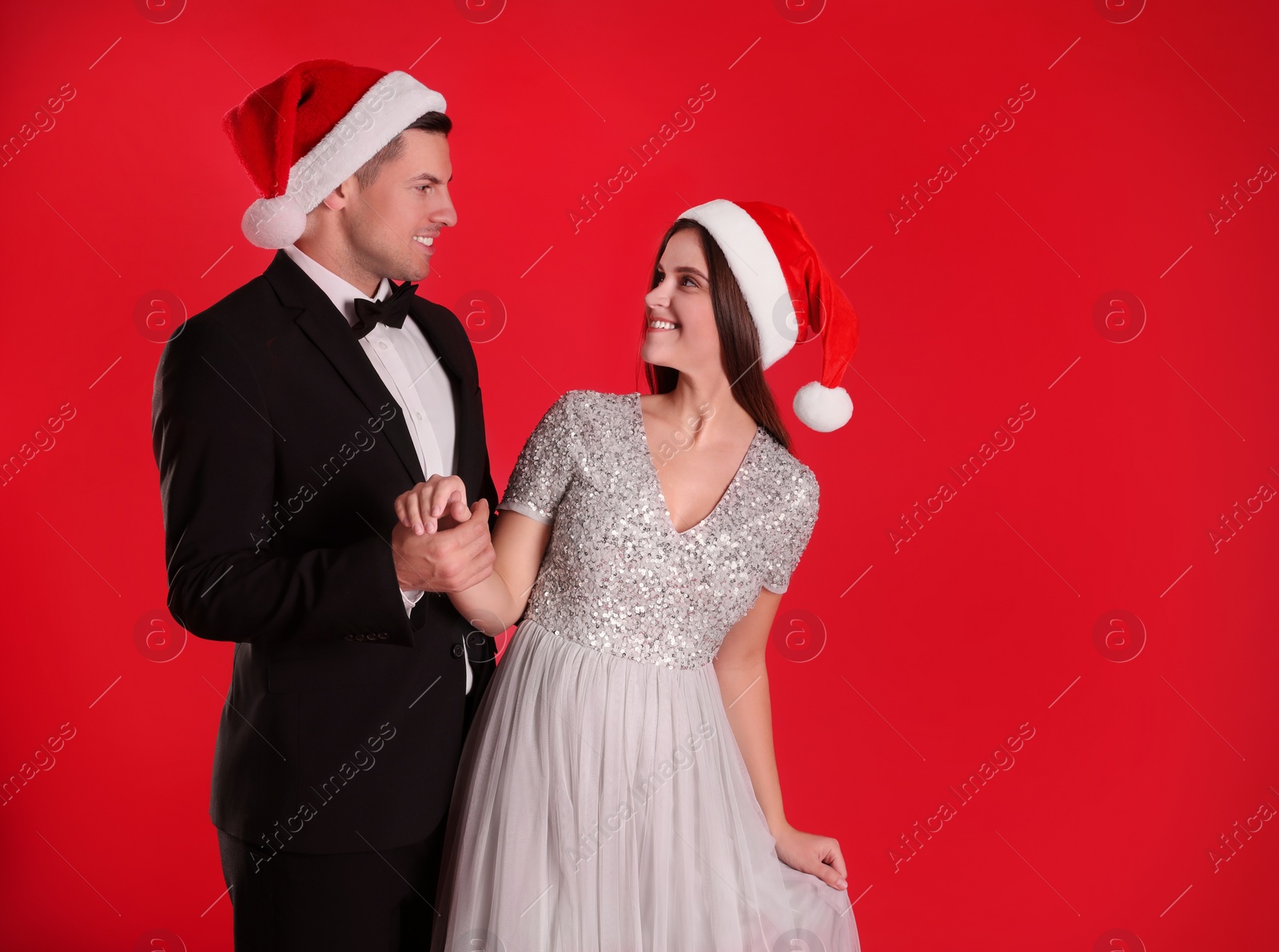 Photo of Beautiful happy couple in Christmas hats on red background. Space for text