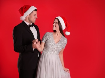 Photo of Beautiful happy couple in Christmas hats on red background. Space for text