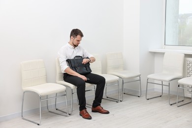 Photo of Man looking at wrist watch and waiting for job interview indoors